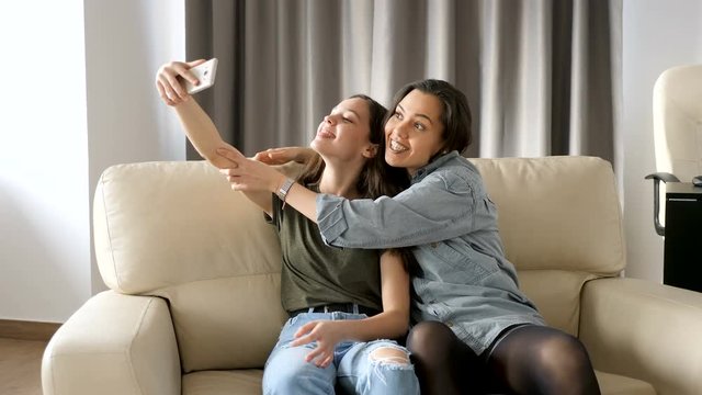 Beautiful sisters in the living room on the couch taking a selfie. They are having fun, laughing and smiling and spending quality time together