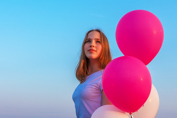 teenage girl in a white tank top with balloons of pink and white against a blue sky with a copy of space on a summer evening