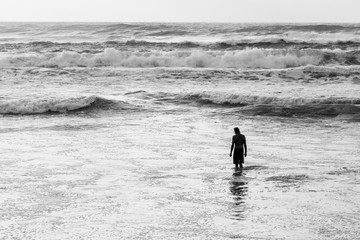 Fototapeta na wymiar Silhouette of a man standing knee deep in ocean waves in black and white