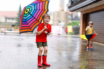 Kid boy wearing red rain boots and walking with umbrella