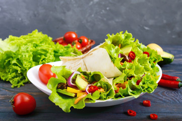 Burrito with chopped meat, avocado, vegetables, hot pepper on a plate on a dark wooden background. Stuffed tortilla. Traditional Mexican appetizer.