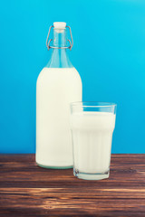 a glass of milk, a bottle of milk on a wooden table on a colored