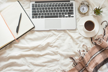 A cup of coffee, a diary and an address book with a laptop and an alarm clock on the bed with a brown plaid. The concept of the morning, and work. Top view, with empty space for inscription