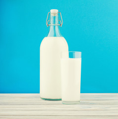 a glass of milk, a bottle of milk on a wooden table on a colored