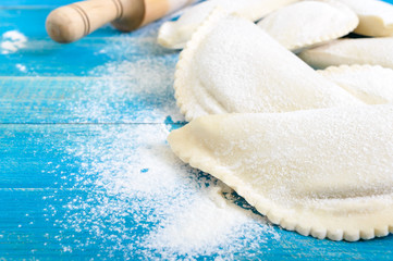 Not fried chebureks in flour on a blue wooden table. Traditional Turkic-Mongolian dish. Frozen semi-finished products.