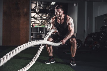 Muscular powerful aggressive man working out with rope in functional training fitness gym