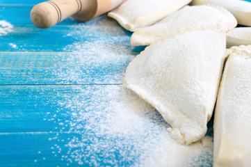 Not fried chebureks in flour on a blue wooden table. Traditional Turkic-Mongolian dish. Frozen semi-finished products.