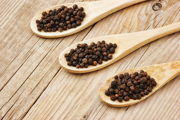 Black pepper in wooden spoon on the old board
