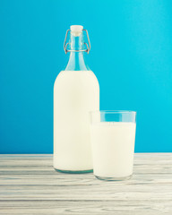 a glass of milk, a bottle of milk on a wooden table on a colored