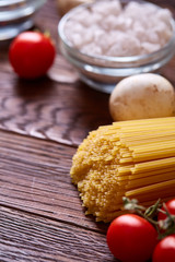 Uncooked pasta, tomatoes and two spoons on wooden background, top view, close-up, selective focus