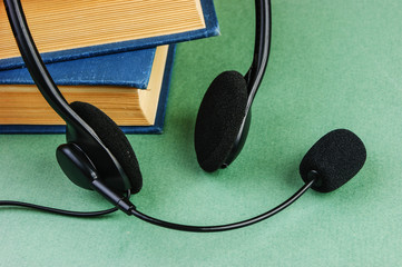 Headphones with a microphone and a stack of books on a green background