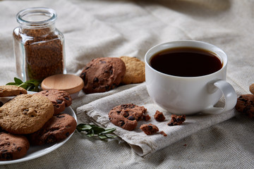 Coffee cup, jar with coffee beans, cookies over homespun tablecloth, selective focus, close-up, top view