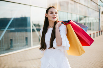 Pretty brunette with long hair walking with shopping bags before a modern glass building