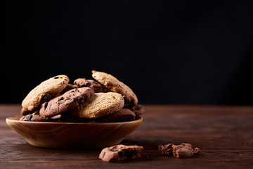 Side view of chocolate chip cookies on a wooden plate over rustic background, selective focus