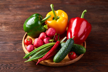 Wooden plate with vegetables for a vegetarian salad on rustic wooden background, close-up, selective focus
