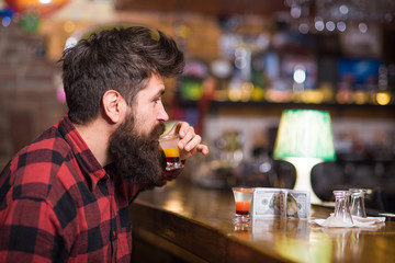 Man with beard drinks alcohol in bar on blurred background.