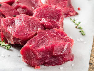 Pieces of raw meat. Raw beef with spices and thyme on white parchment paper on wooden rough rustic background, side view, close up.