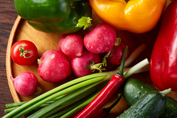 Wooden plate with vegetables for a vegetarian salad on rustic wooden background, close-up, selective focus