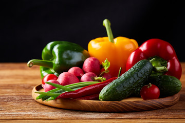 Wooden plate with vegetables for a vegetarian salad on rustic wooden background, close-up, selective focus