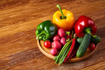 Wooden plate with vegetables for a vegetarian salad on rustic wooden background, close-up, selective focus