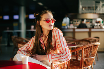 Pretty fashion model in red sunglasses works with her tablet sitting at the cafe in the rays of sunset
