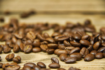 Coffee beans spilled onto a wood table with the focus on the beans near the viewer.