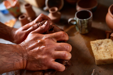 Hands of male potter molding a clay in pottery workshop, close-up, selective focus
