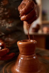 Close-up hands of a male potter in apron making a vase from clay, selective focus