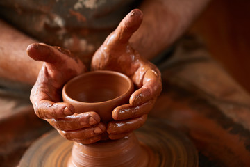 Fototapeta na wymiar Close-up hands of a male potter in apron molds bowl from clay, selective focus