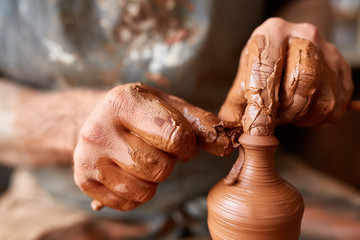 Close-up hands of a male potter in apron molds bowl from clay, selective focus