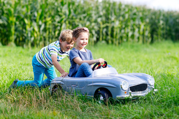 Naklejka na ściany i meble Two happy children playing with big old toy car in summer garden, outdoor