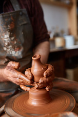 Close-up hands of a male potter in apron molds bowl from clay, selective focus