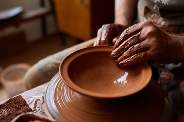 Close-up hands of a male potter in apron molds bowl from clay, selective focus