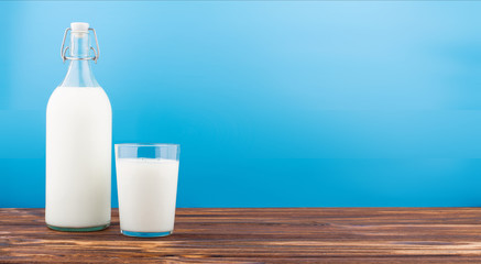 a glass of milk, a bottle of milk on a wooden table on a colored background