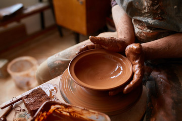 Close-up hands of a male potter in apron molds bowl from clay, selective focus