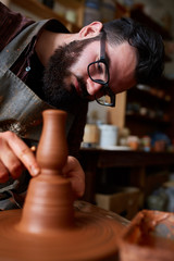 Fototapeta na wymiar Portrait of a male potter in apron molds bowl from clay, selective focus, close-up