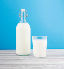 a glass of milk, a bottle of milk on a wooden table on a colored background