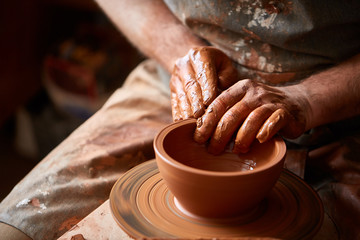 Close-up hands of a male potter in apron molds bowl from clay, selective focus