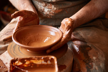 Close-up hands of a male potter in apron molds bowl from clay, selective focus