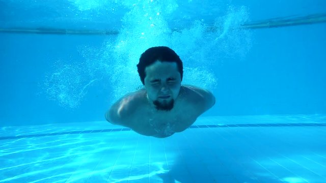 Man is swimming under water. It releases air from nose. Pool. Underwater photography. Slow motion.
