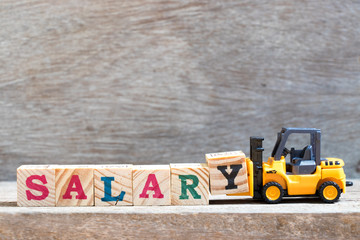 Toy forklift hold letter block Y to complete word salary on wood background