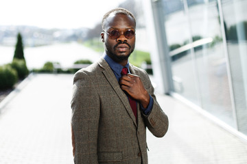 Stylish African American black businessman in round sunglasses poses before a modern glass building outside