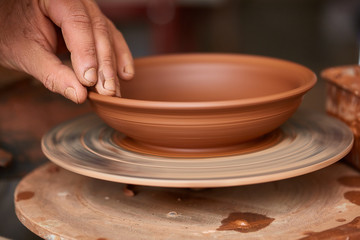 Close-up hands of a male potter in apron molds bowl from clay, selective focus