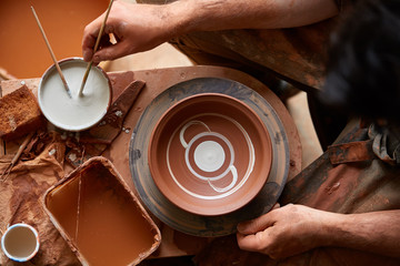 A potter paints a clay plate in a white in the workshop, top view, close-up, selective focus.