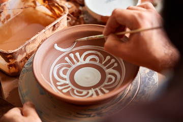 A potter paints a clay plate in a white in the workshop, top view, close-up, selective focus.