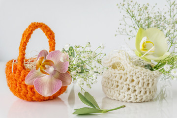 Obraz na płótnie Canvas Close-up of wicker crochet baskets in orange and beige with spring flowers, gentle orchid in pink and pale yellow on white background. Shallow depth of focus, spa concept.