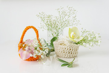 Close-up of wicker crochet baskets in orange and beige with spring flowers, gentle orchid in pink and pale yellow on white background. Shallow depth of focus, spa concept.