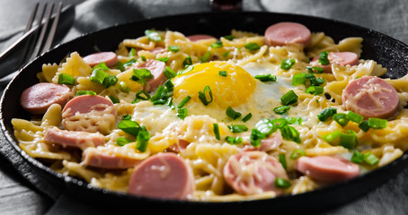 fried eggs with pasta farfalle, sausage and cheese in a frying pan on wooden table