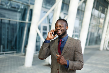 Stylish African American black businessman talks on his smartphone standing before a modern glass building outside