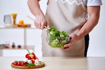 Man cooking at kitchen making healthy vegetable salad, close-up, selective focus.